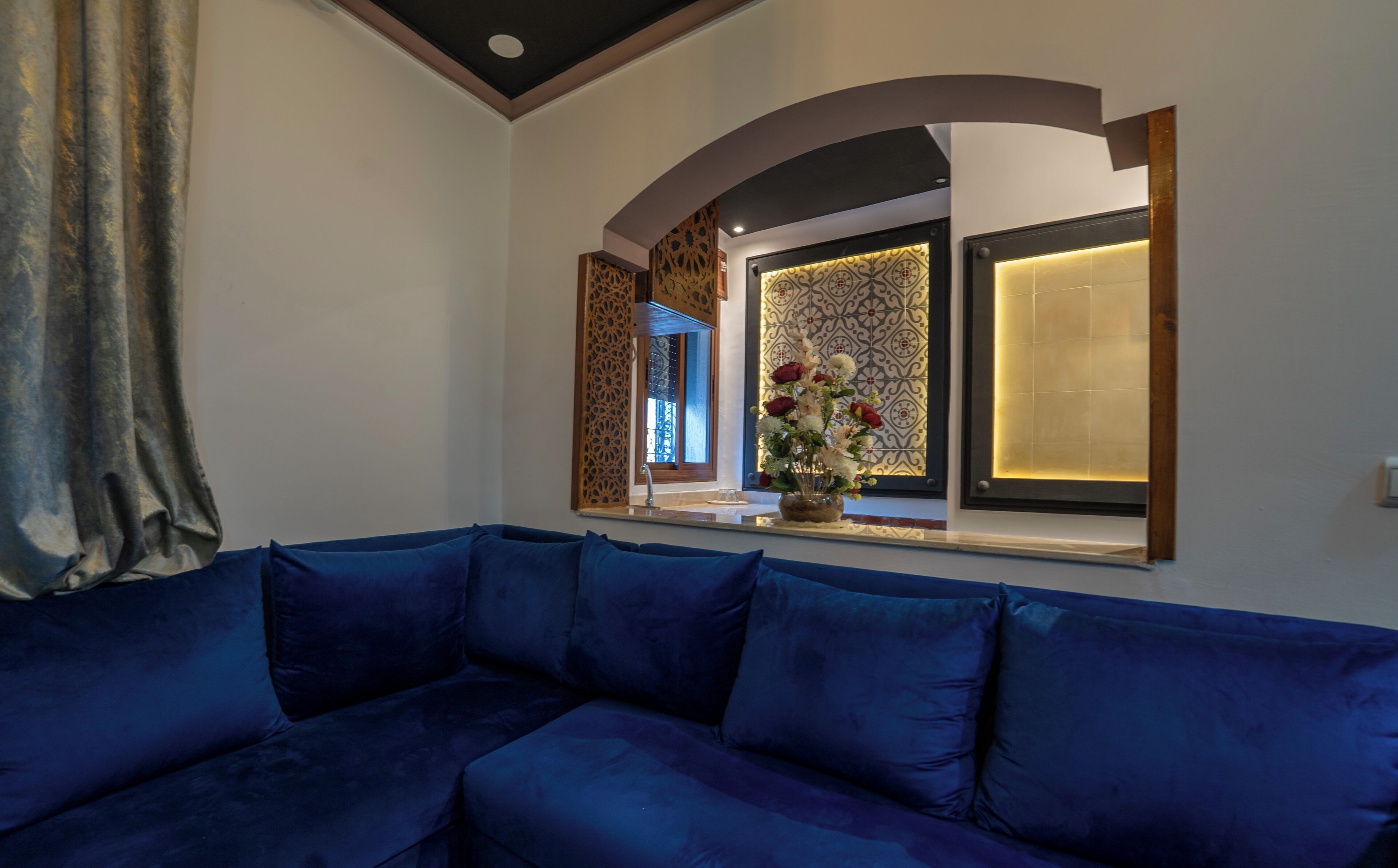 A modern living room with a blue sofa, decorative wall panels, and a vase with flowers.