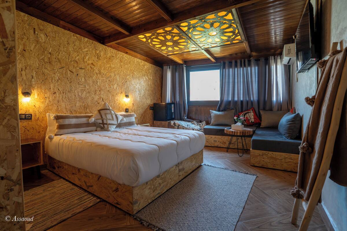 A cozy bedroom with a wooden bed, a sofa, and a decorative ceiling.