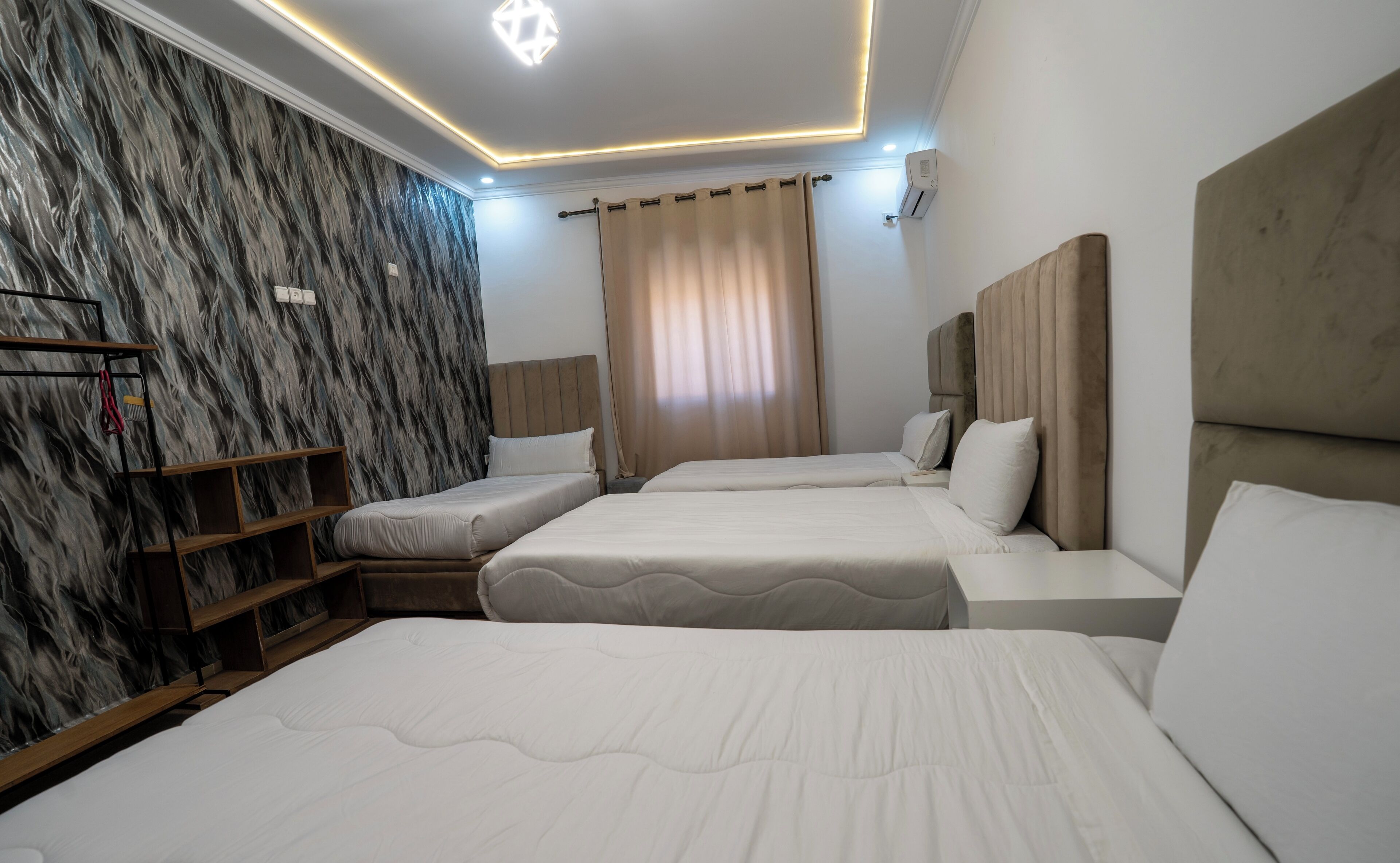 A hotel room with three beds, a marble-patterned wall, and a modern ceiling design.