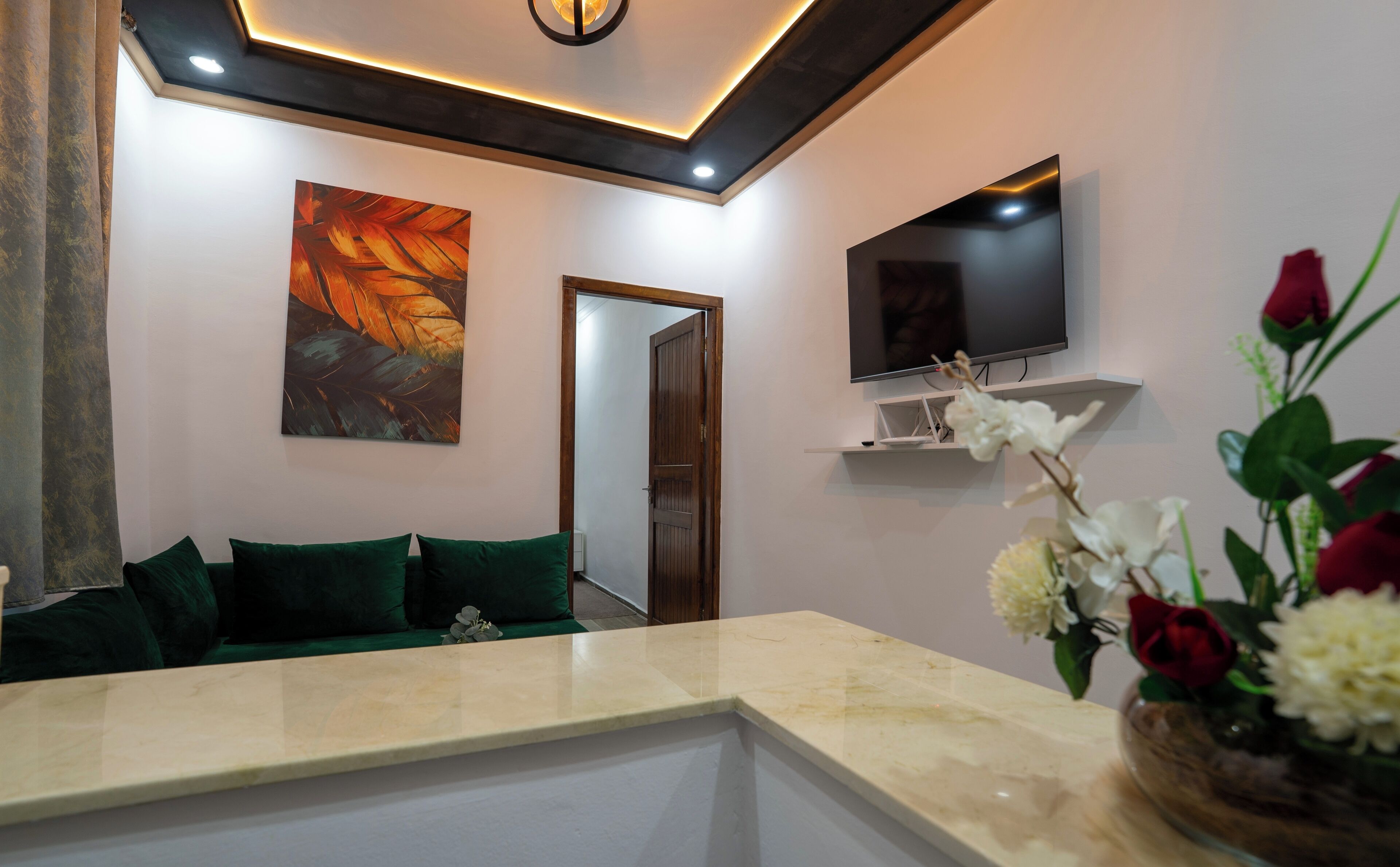 A modern living room with a marble countertop, green sofa, artwork, a flat-screen TV, and a vase with flowers.