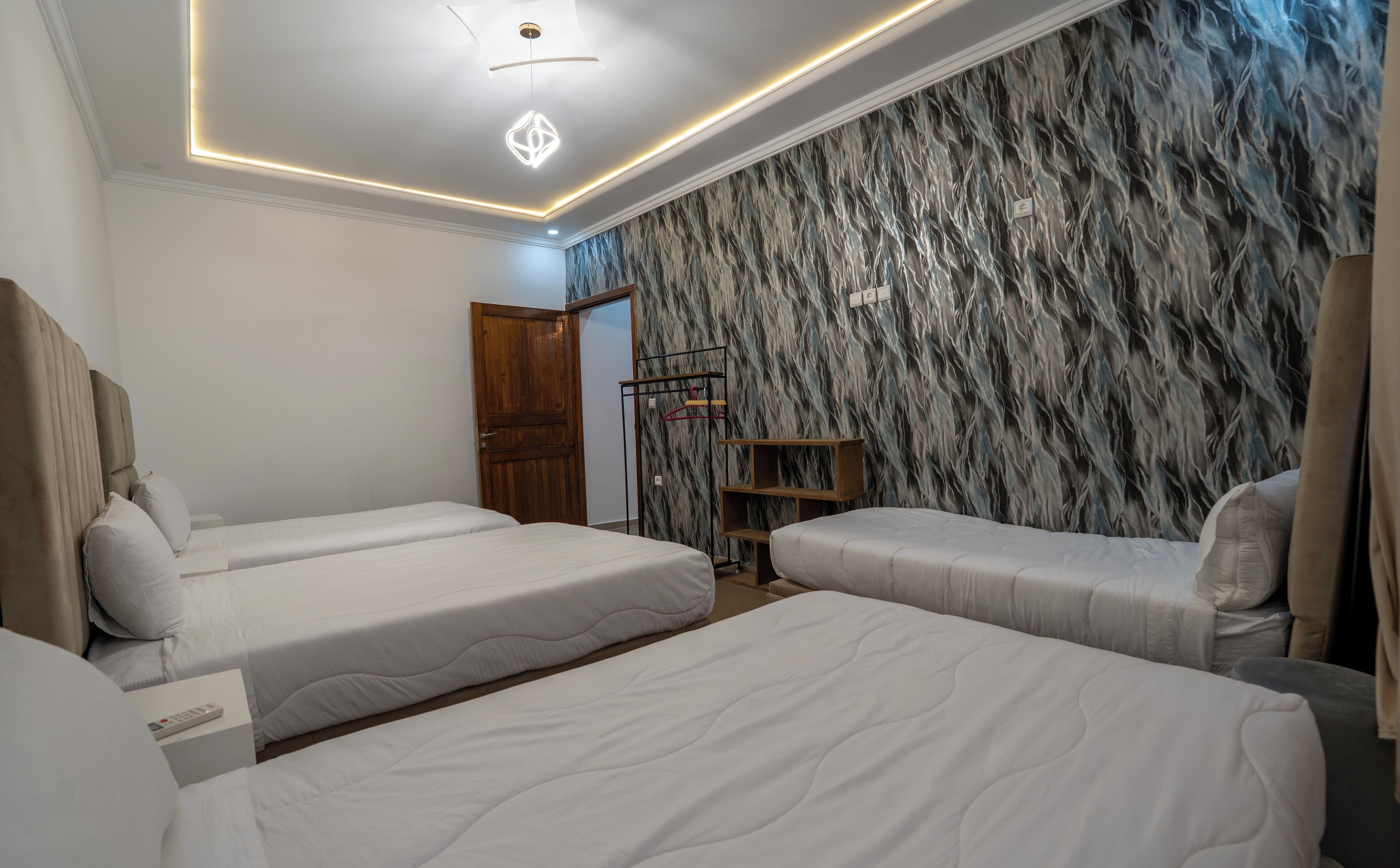 A hotel room with three beds, a wooden wardrobe, a clothing rack, and a marble-patterned wall.