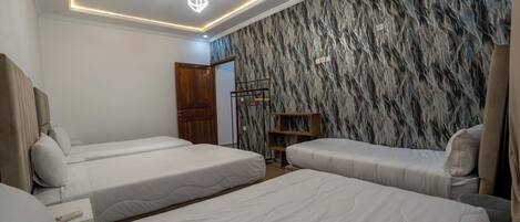 A hotel room with three beds, a wooden wardrobe, a clothing rack, and a marble-patterned wall.