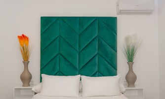 Un dormitorio con un cabecero tapizado en color turquesa, ropa de cama blanca y dos jarrones con plantas secas sobre las mesitas de noche.