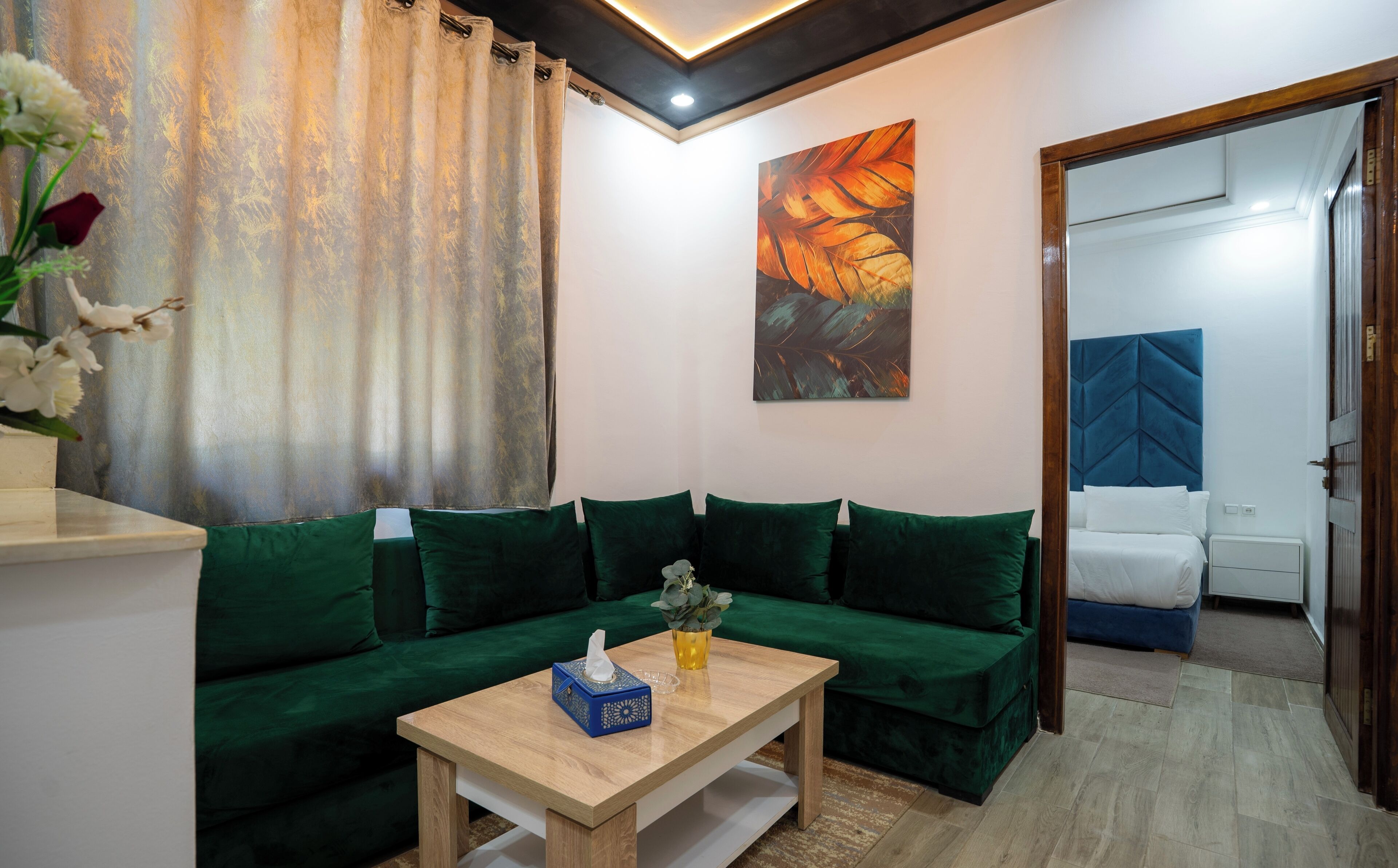 A modern living room with a green sofa, a wooden coffee table, and a painting on the wall.