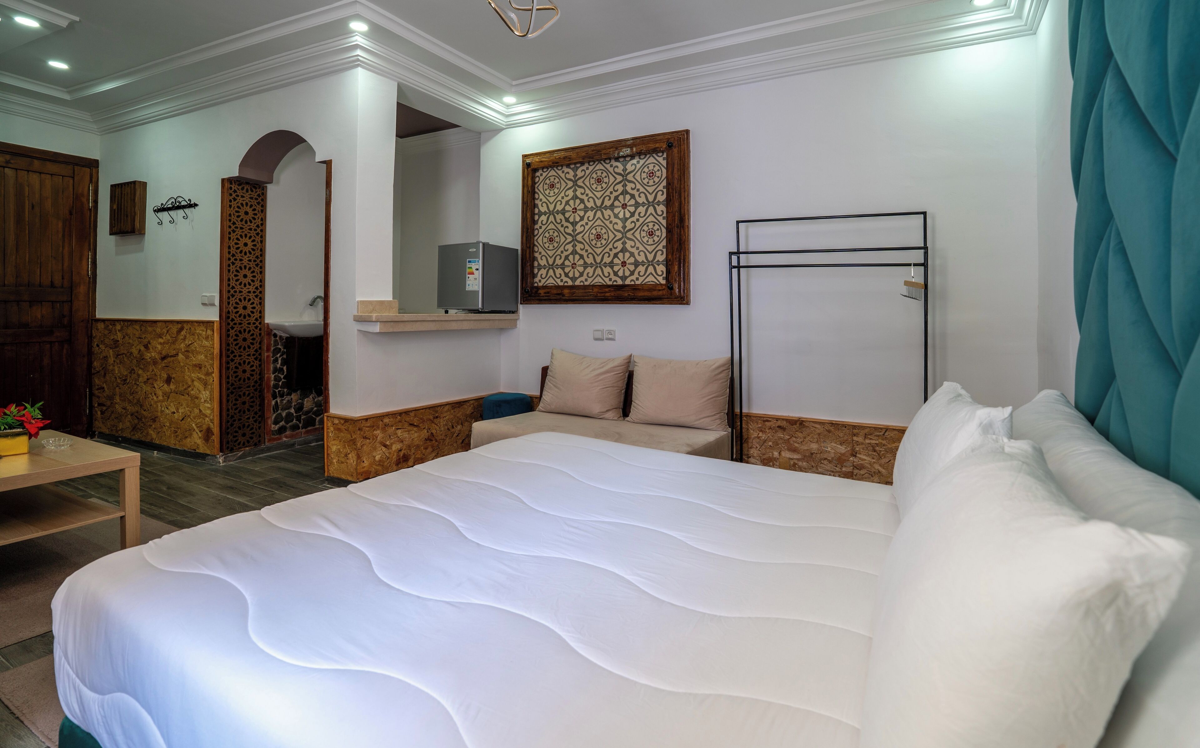 Une chambre d’hôtel avec un grand lit, un petit bureau, un miroir, une télévision et une salle de bain visible à travers une arche.