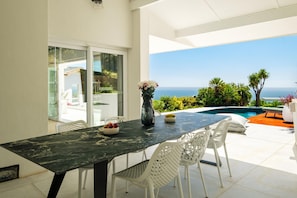 A dining area with a table, chairs, and a view of the ocean. - Camps Bay Villa w Pool Gym Studio Aqua Terra (Cape Town)