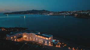 Ein Küstengebäude mit mehreren Ebenen, einem Schwimmbad und Blick auf das Meer und eine entfernte Stadt.