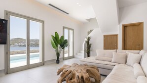 Ein modernes Wohnzimmer mit einem großen weißen Sofa, einem Holztisch und Meerblick durch raumhohe Fenster.