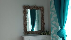 A white dresser with a mirror above it, a small plant on top, and a teal curtain on the right.