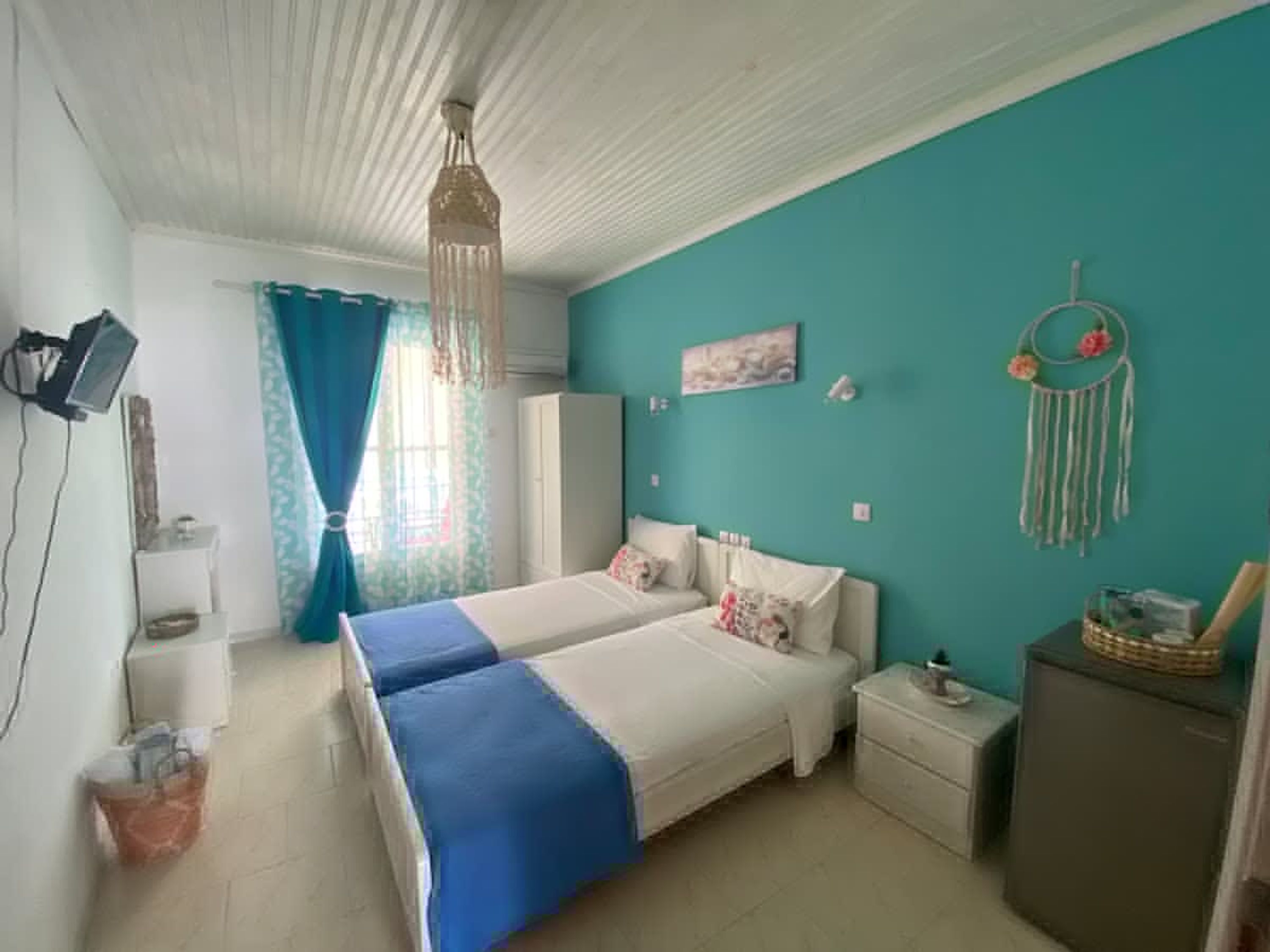 A bedroom with two beds, a wardrobe, a desk, and a wall-mounted TV.