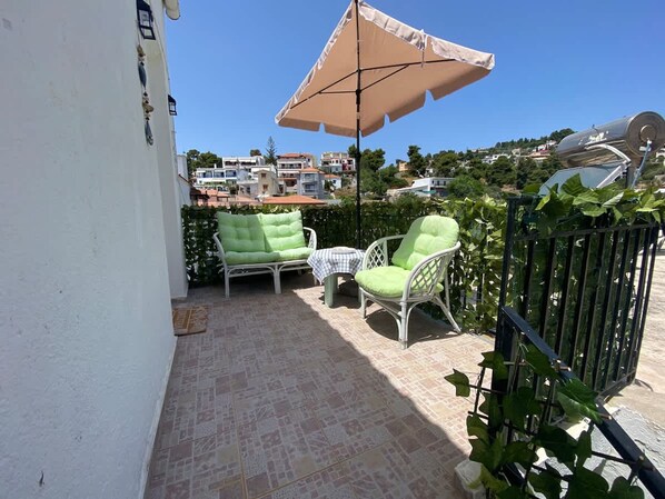 A patio with two wicker chairs, a table, and a large umbrella.