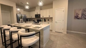 Una cocina moderna con una isla grande, armarios blancos e iluminación colgante.