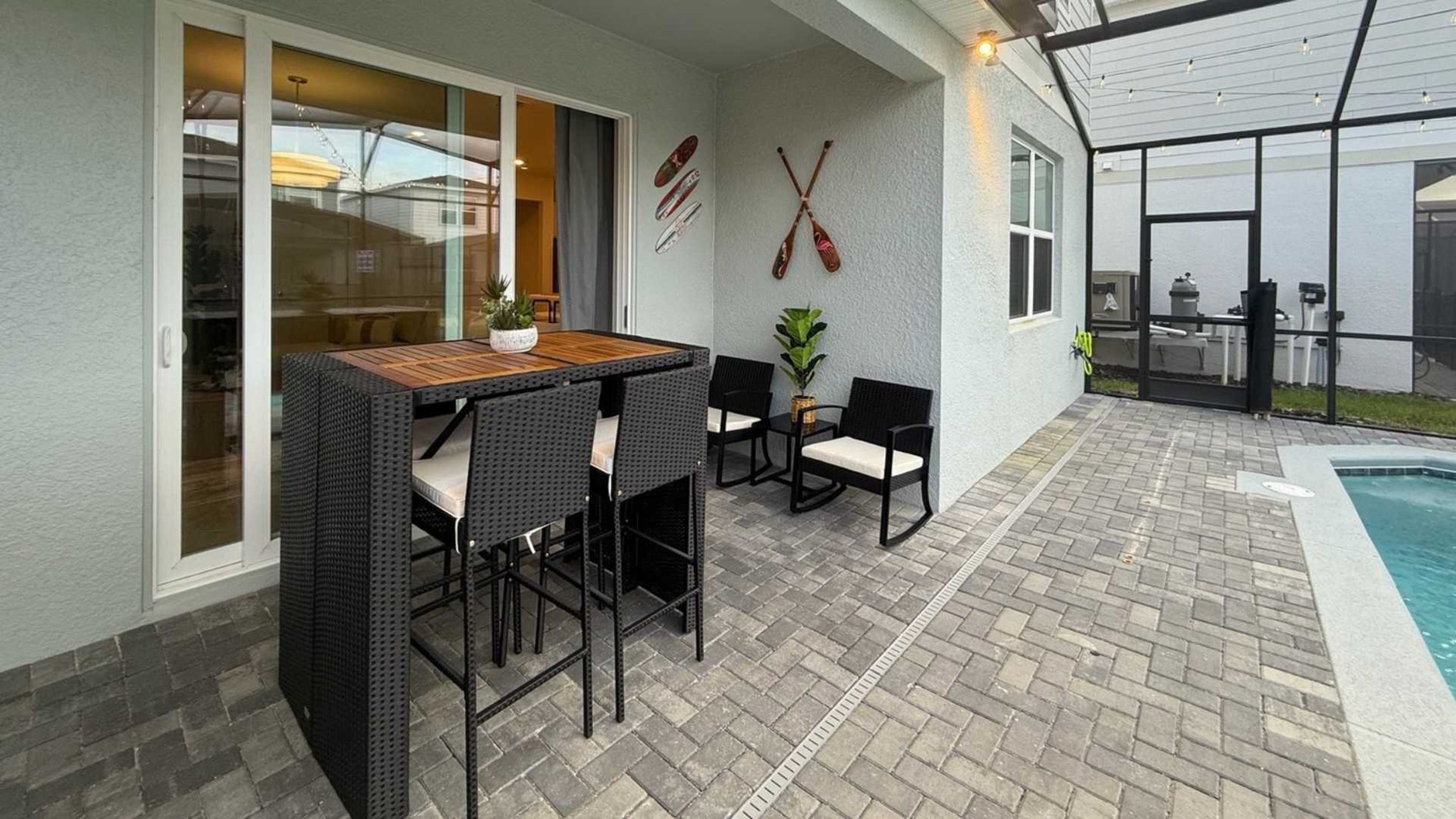 An outdoor patio with a pool, a table with chairs, and a sliding glass door leading to a room.