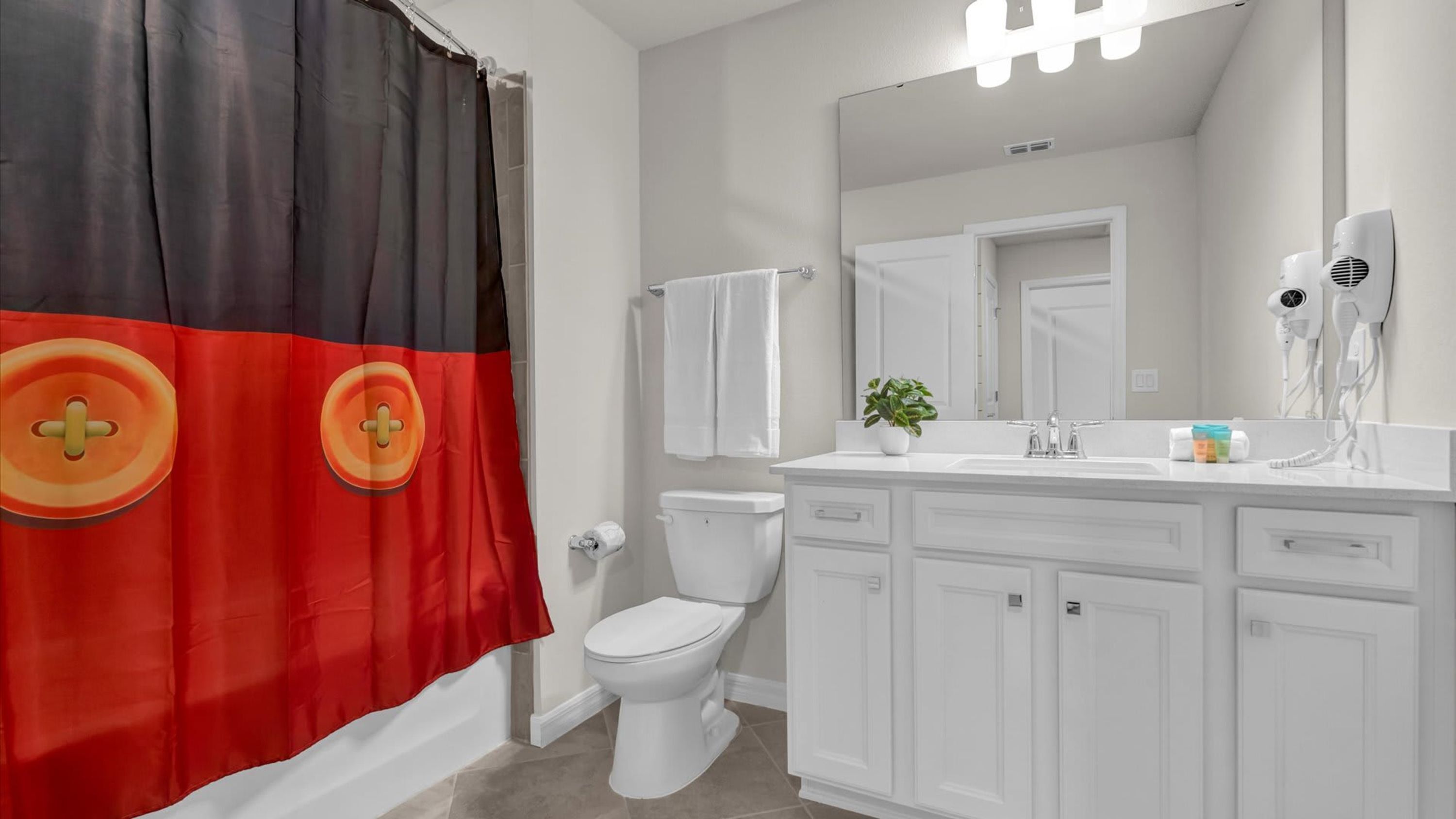 A bathroom with a toilet, a sink with a mirror, a shower curtain, and a towel rack.