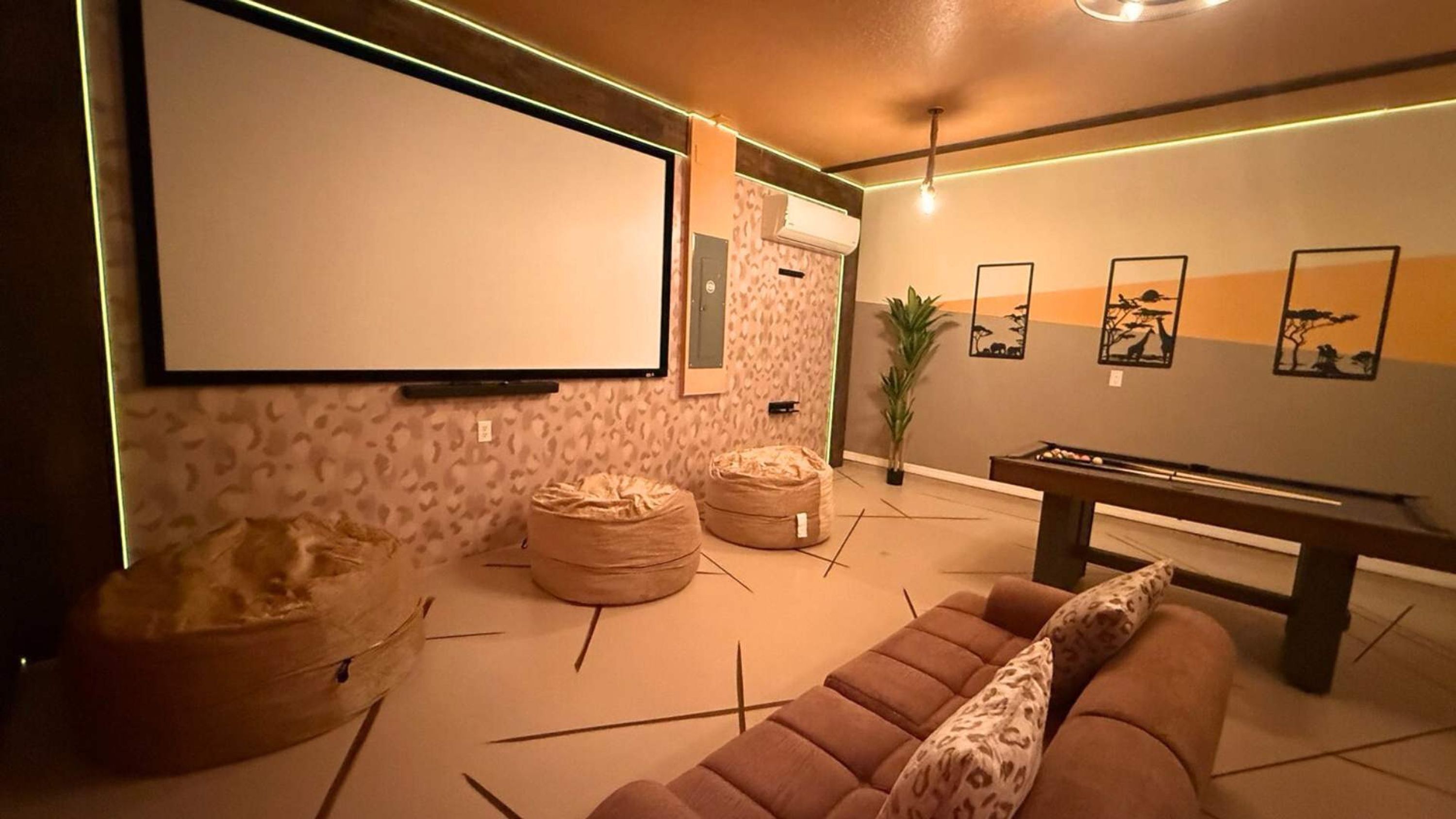 A modern living room with a large flat-screen TV, two bean bags, a pool table, and leopard-print cushions.