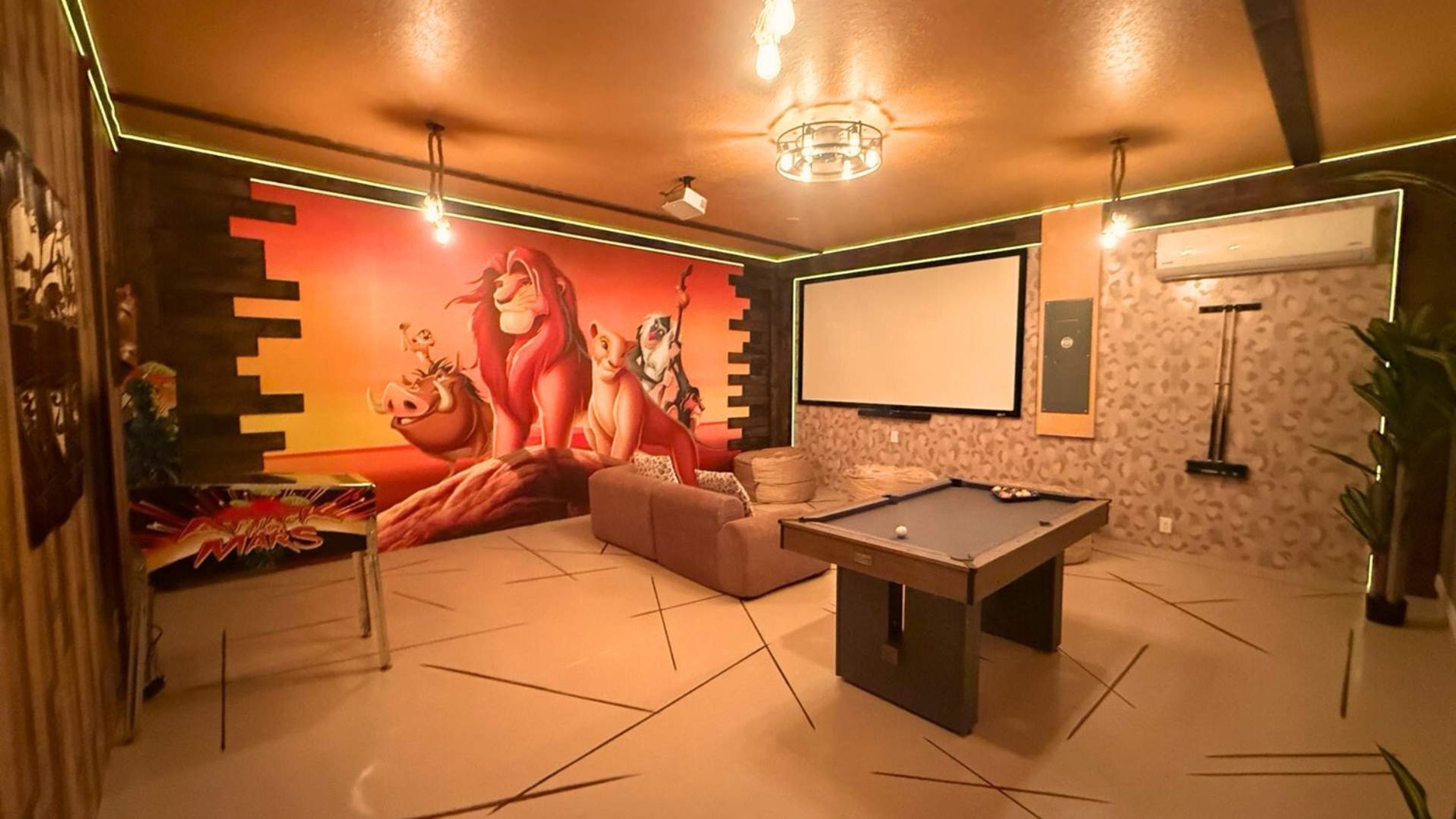 Ein Raum mit Poolbillard, einer Couch, einem Wandgemälde und einer Projektionsleinwand.