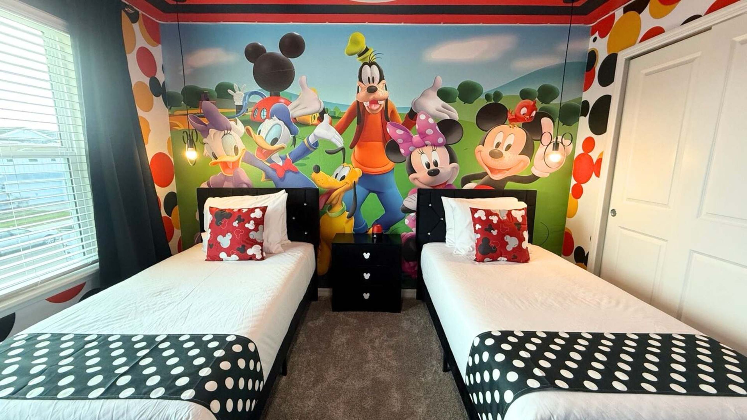 Une chambre d’enfant avec deux lits, chacun décoré avec de la literie aux motifs de Mickey et de Minnie Mouse, et une grande fresque représentant des personnages de Disney sur le mur.
