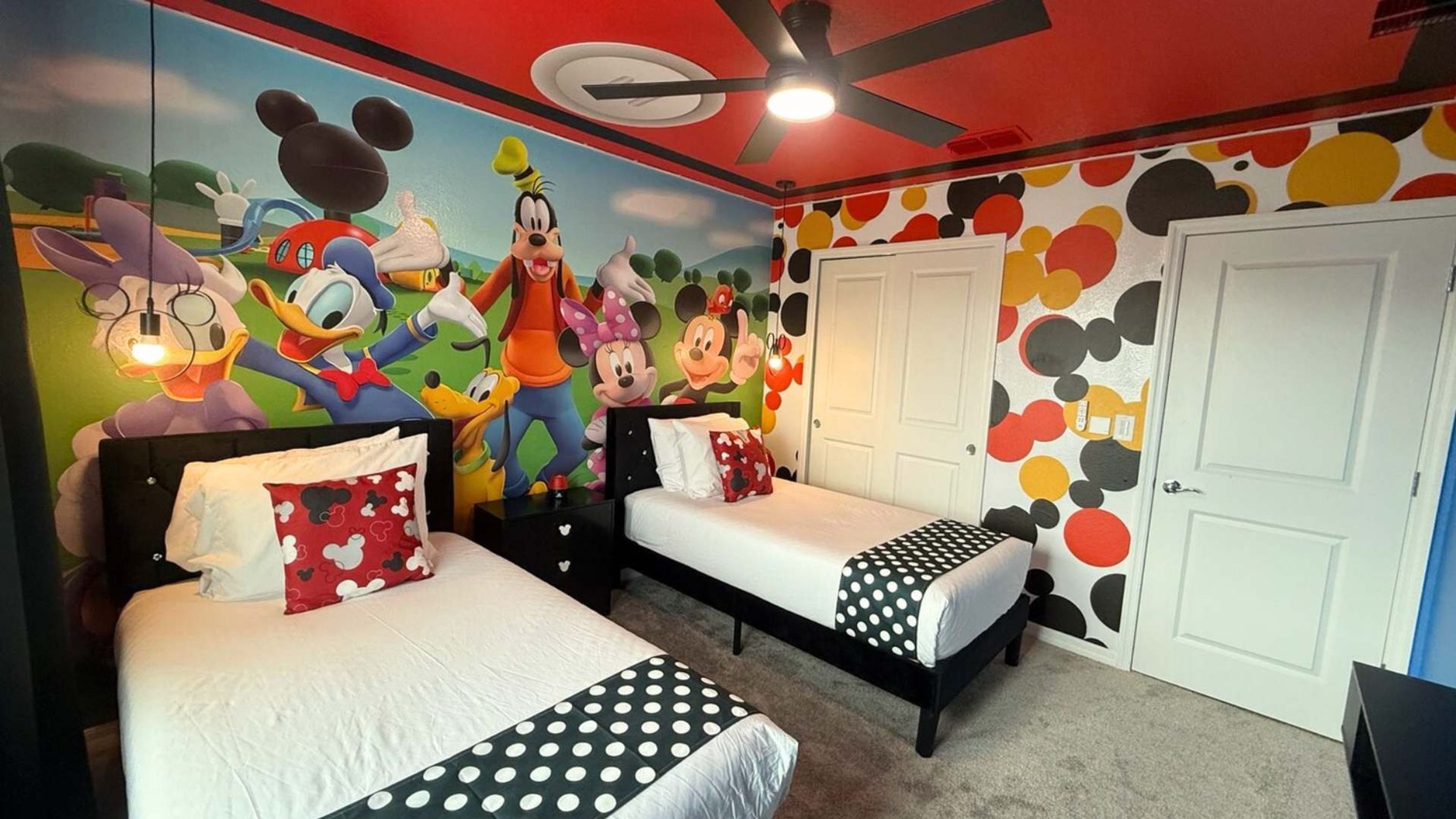 Quarto infantil com murais do Mickey e Minnie Mouse, duas camas e um ventilador de teto.