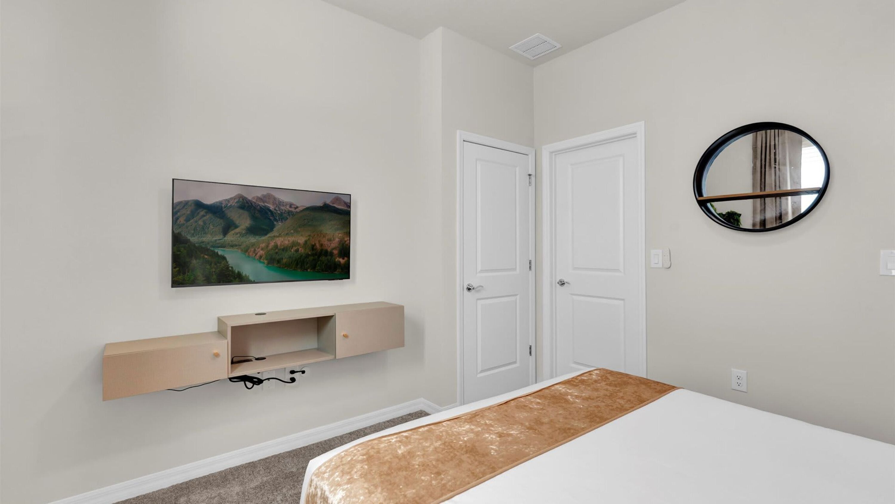 Una camera da letto con un letto, una TV a parete, una porta e uno specchio rotondo.