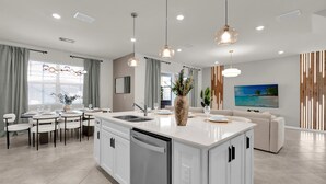 Una cocina moderna con una isla central, armarios blancos e iluminación colgante.