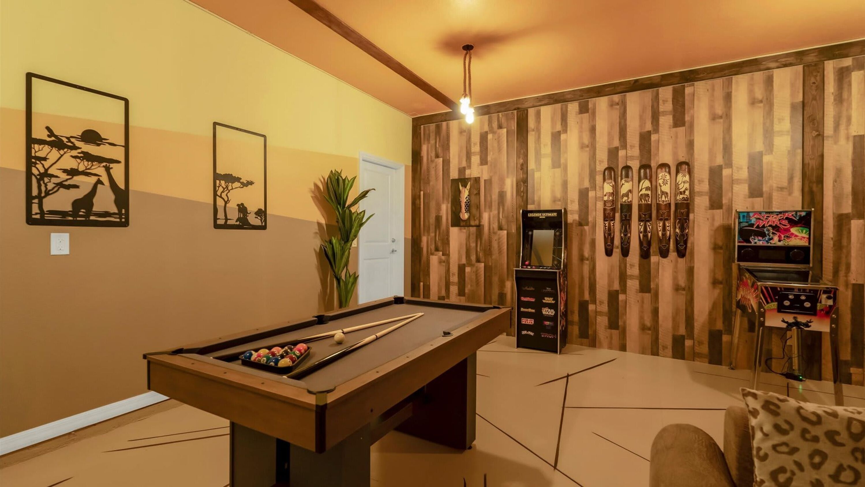 A pool table in a room with wooden panel walls, a ceiling light, and framed artwork.