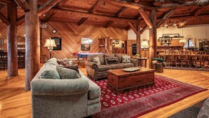 A spacious loft-style living area with a high ceiling, wooden beams, and a cozy fireplace. - Great Camp Hollywood Hills (Old Forge)