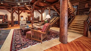 A log cabin interior with a cozy living area featuring a fireplace, wooden furniture, and a staircase leading to an upper level. - Great Camp Hollywood Hills (Old Forge)