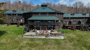 A large log cabin with a green roof, multiple balconies, and a patio area with outdoor seating. - Great Camp Hollywood Hills (Old Forge)