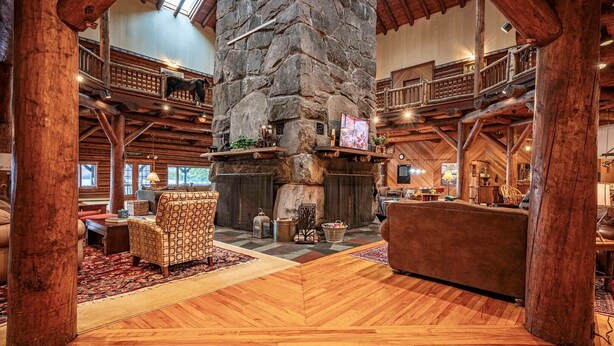A spacious lodge interior with a stone fireplace, wooden beams, and a high ceiling. - Great Camp Hollywood Hills (Old Forge)