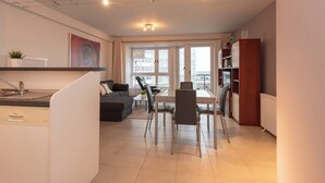 Un appartement moderne comprenant une cuisine, un coin repas et un salon. Il dispose d’une grande fenêtre qui laisse entrer la lumière naturelle et offre une vue sur la ville.