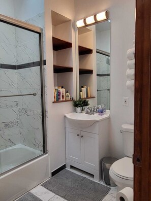 Un baño con cabina de ducha de vidrio, un lavamanos blanco con espejo y un inodoro.