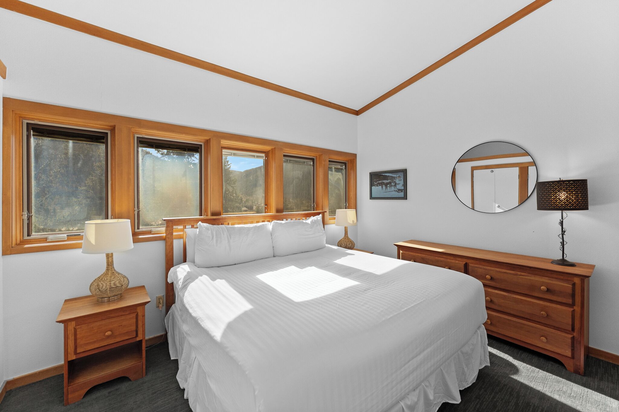 Une chambre à coucher avec un grand lit, une tête de lit en bois, deux tables de chevet avec des lampes, une commode et un miroir au mur.