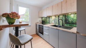 A modern kitchen with grey cabinets, a black sink, and a window overlooking a forest. - Garden 5 - Apartment 4 (Braunlage)