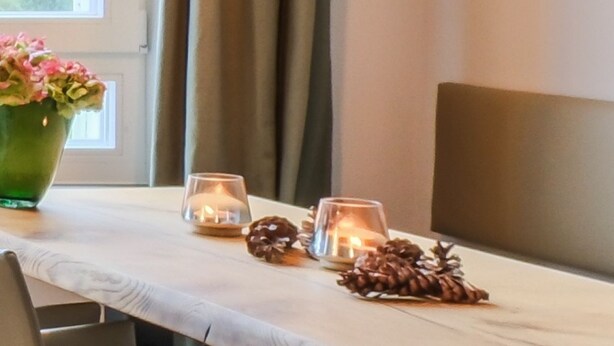 A table with a vase of flowers, two candles, and pine cones. - Garden 5 - Apartment 4 (Braunlage)