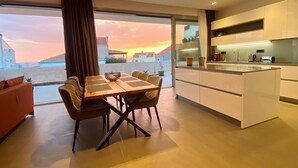 A modern kitchen with a large island, a dining area with a table and chairs, and a view of the sunset over the sea.