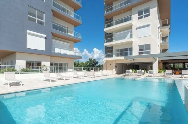 Un hotel moderno con piscina, varios balcones y sillones de sol.