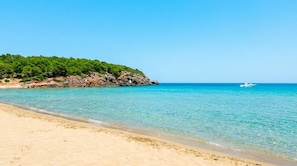 Une plage à l’eau turquoise et limpide, un rivage sablonneux et un promontoire rocheux parsemé de végétation.