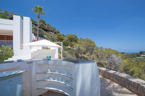 Un área de cocina exterior moderna con un enfriador de vinos integrado y una vitrina de vidrio.