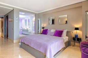 Habitación de hotel con una cama grande, una mesita de noche, un espejo y un baño visible a través de una puerta abierta.