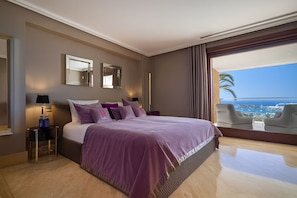 Une chambre d’hôtel avec un grand lit, une vue sur la mer et un balcon équipé de chaises.