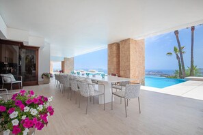 Un espace repas extérieur moderne avec vue sur la piscine, des piliers en pierre et un ciel dégagé.
