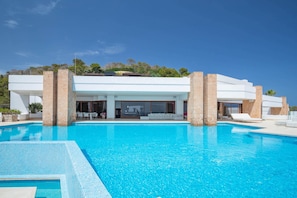 A modern poolside area with a clear blue pool, stone pillars, and a covered seating area.