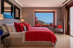 Une chambre d’hôtel avec un grand lit, un bureau et une chaise. Il y a une fenêtre donnant sur la mer.