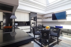 Una cocina moderna con una isla central, un comedor con una mesa redonda y sillas, y un televisor de pantalla plana montado en la pared.