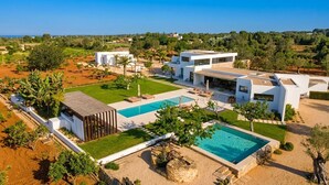 Eine moderne Villa mit Swimmingpool, mehreren Sitzbereichen im Freien und einem gepflegten Garten.