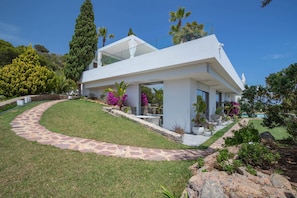 Une maison moderne dotée d’un patio couvert, d’un chemin en pierre et d’un aménagement paysager luxuriant.
