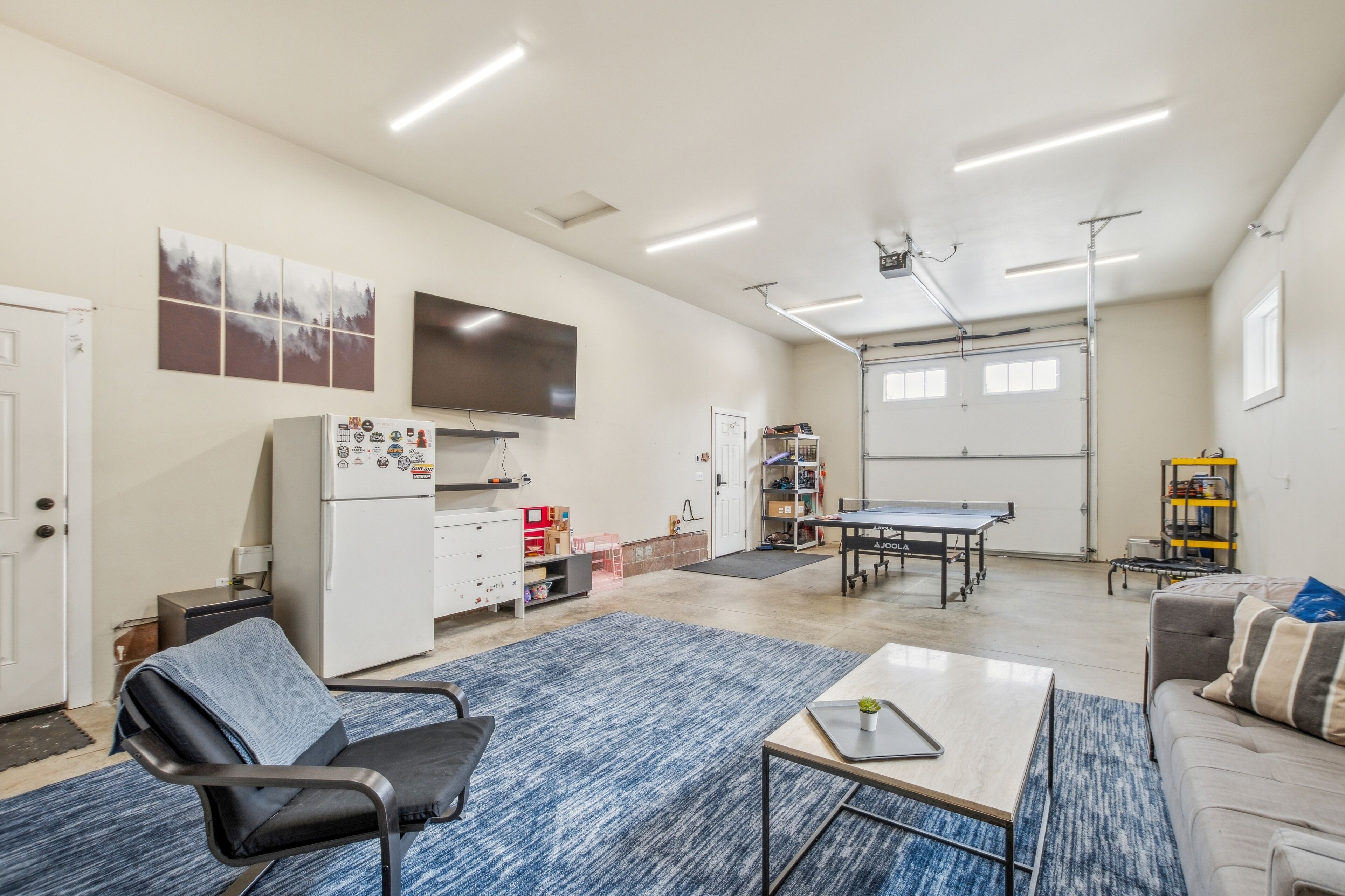 A spacious living area with a large flat-screen TV, a ping pong table, and a cozy seating area with a sofa and a chair.