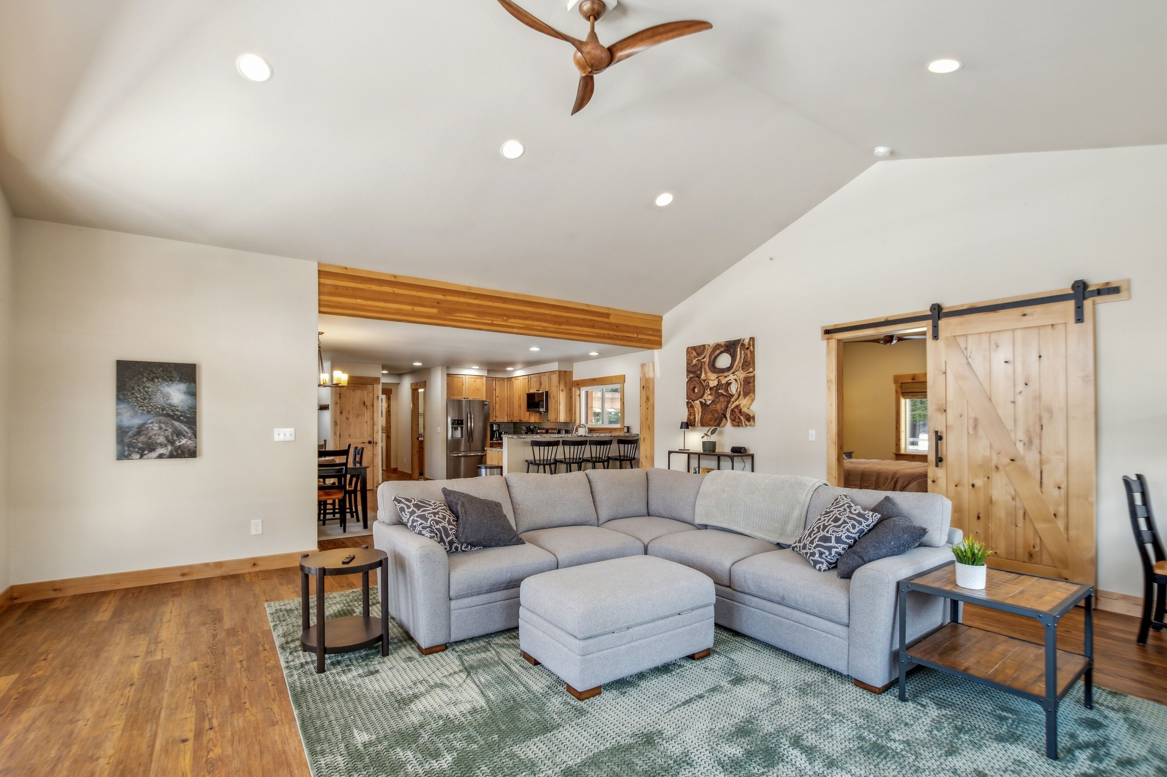 A spacious living room with a sectional sofa, a small side table, and a wooden ceiling fan.