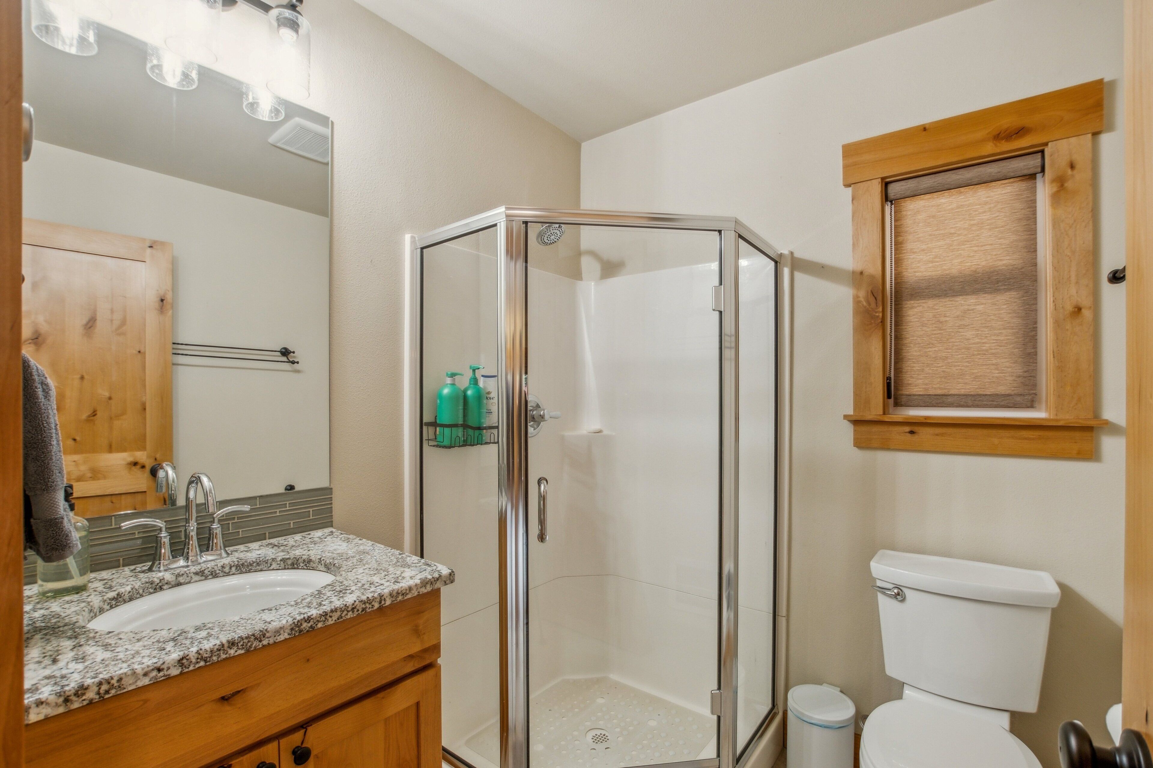 Une salle de bain avec une douche à parois de verre, un lavabo avec un plan de travail en granit et des toilettes.