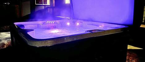 A hot tub with a blue light, a window, and a wooden structure in the background.